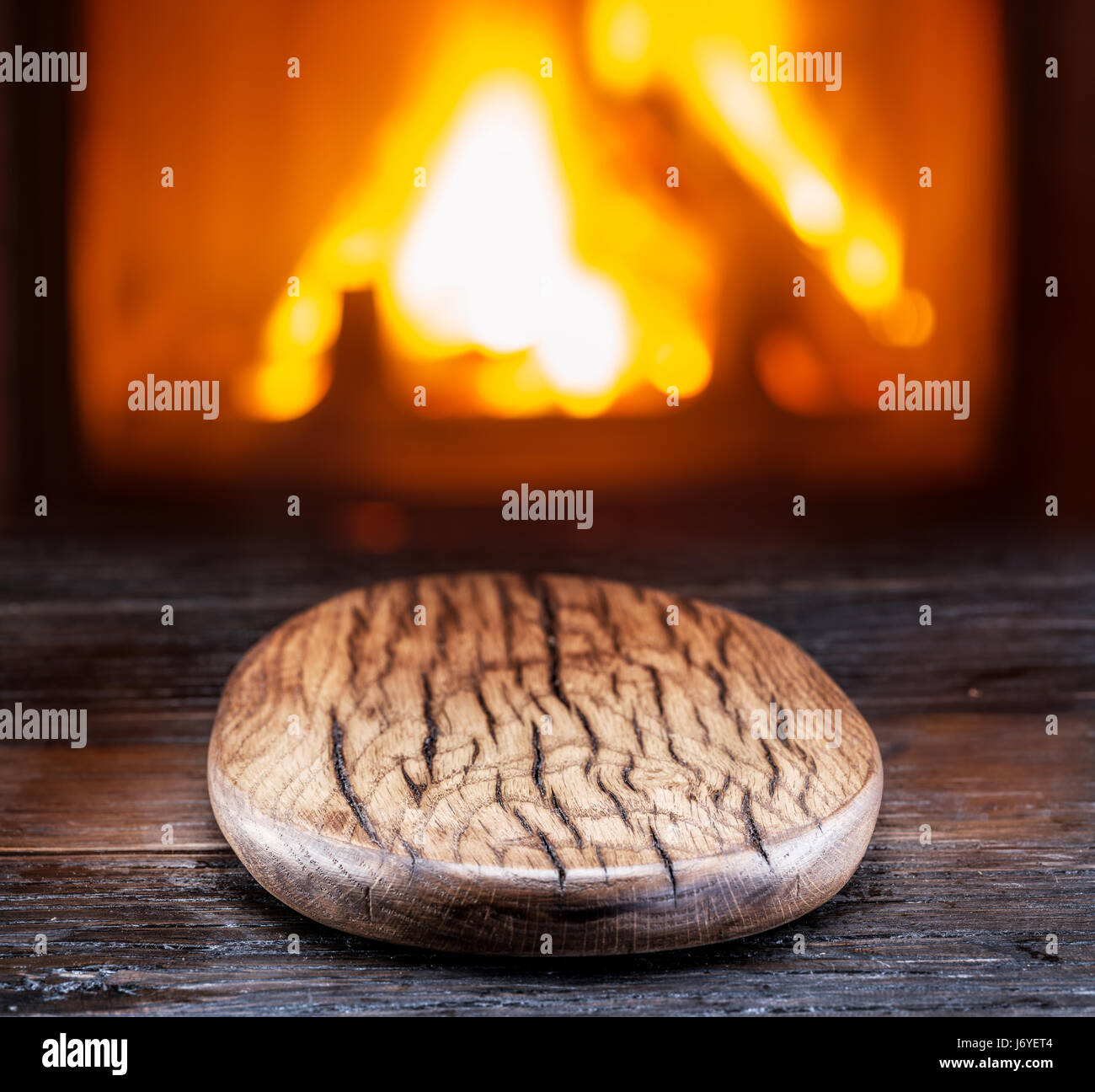 Leere Schneidebrett aus Holz auf dem Holztisch. Helles Feuer im Kamin im Hintergrund. Stockfoto