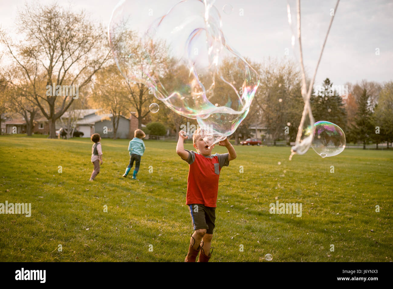 Drei Kinder spielen mit riesige Seifenblasen in einem park Stockfoto
