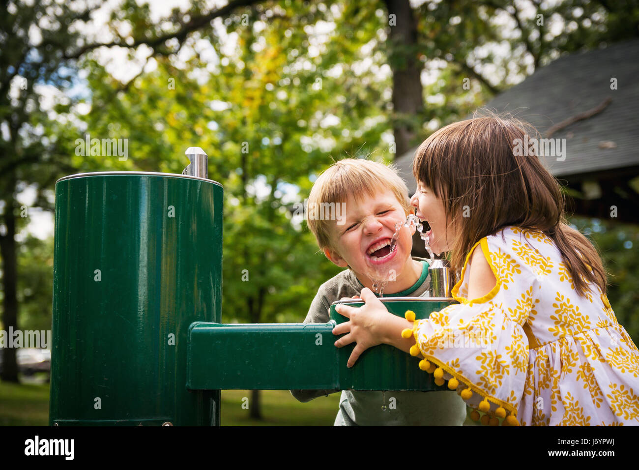 Zwei glückliche Kinder, die Wasser aus einem Brunnen trinken Stockfoto