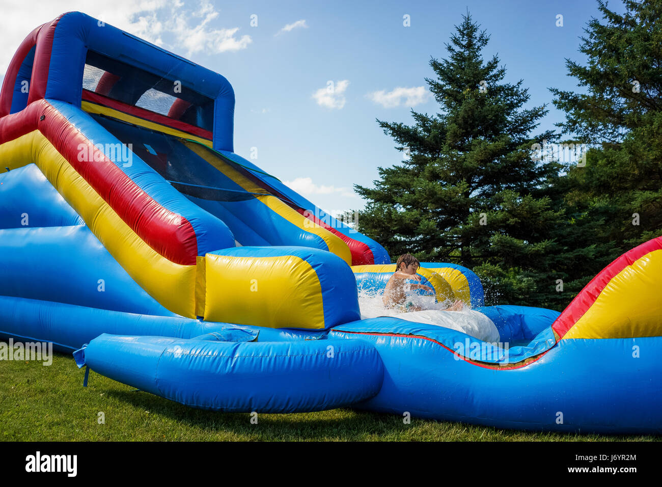 Junge spielt auf aufblasbaren Wasserrutsche Stockfoto