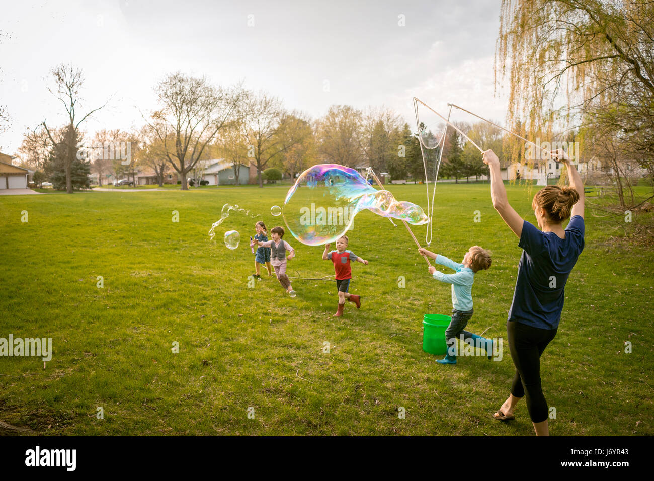 Mutter und vier Kinder spielen mit Riesenseifenblasen Stockfoto