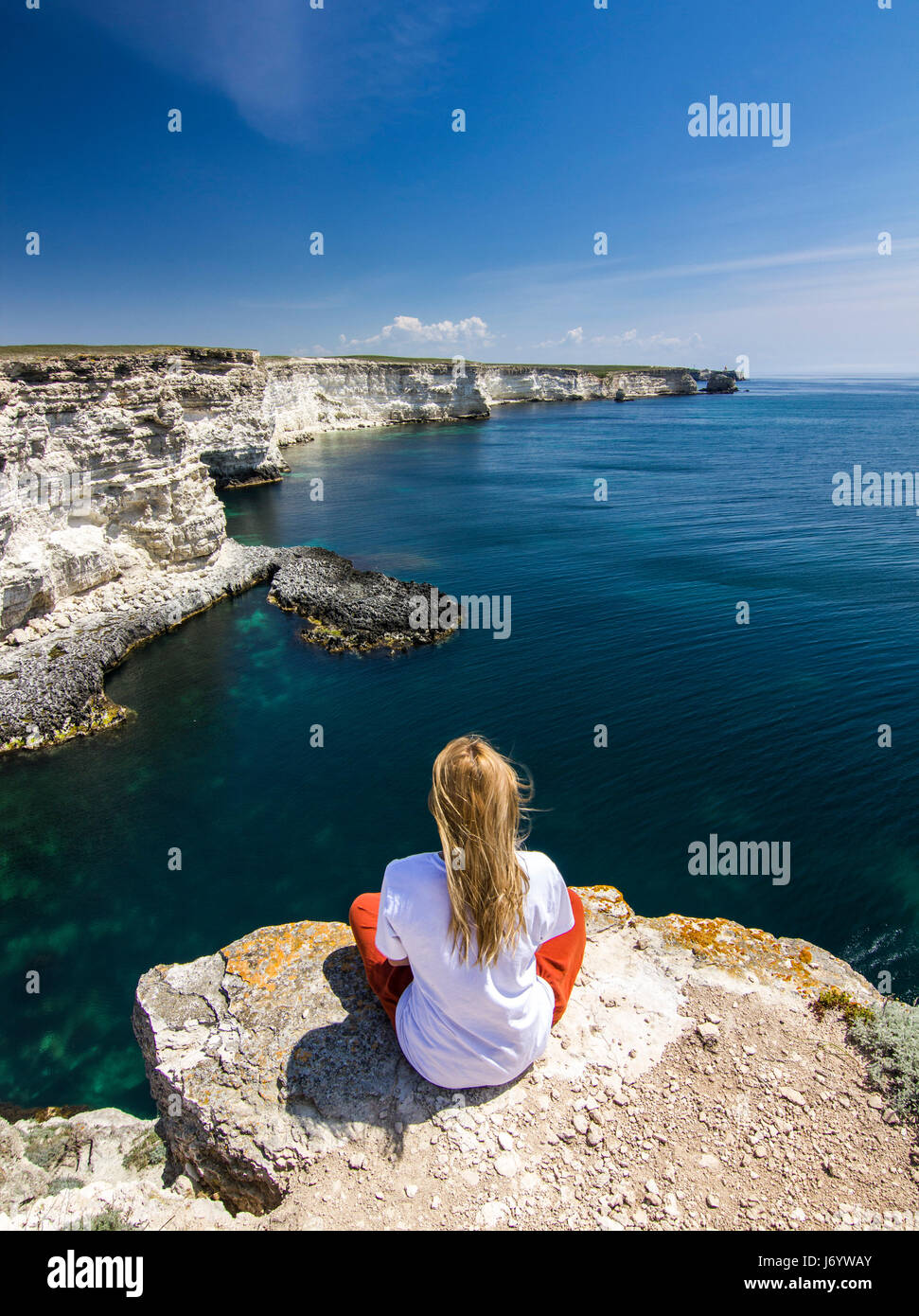 Mädchen in weißen t-Short sitzt auf einer Klippe in der Nähe von Meeresbucht Stockfoto