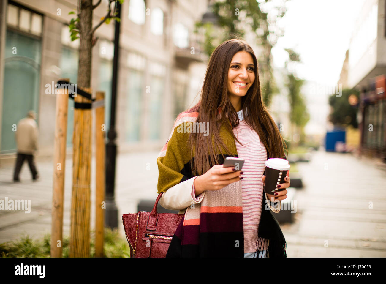 Junge Geschäftsfrau zu Fuß auf der Straße mit Kaffee und Zelle Telefon in der hand Stockfoto