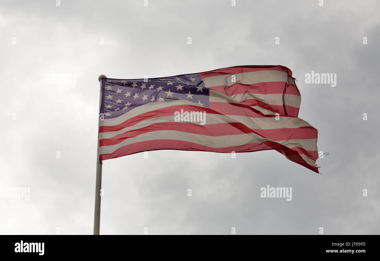 Verblasst und zerfetzt amerikanische Flagge winken gegen ein bewölkter Himmel Stockfoto