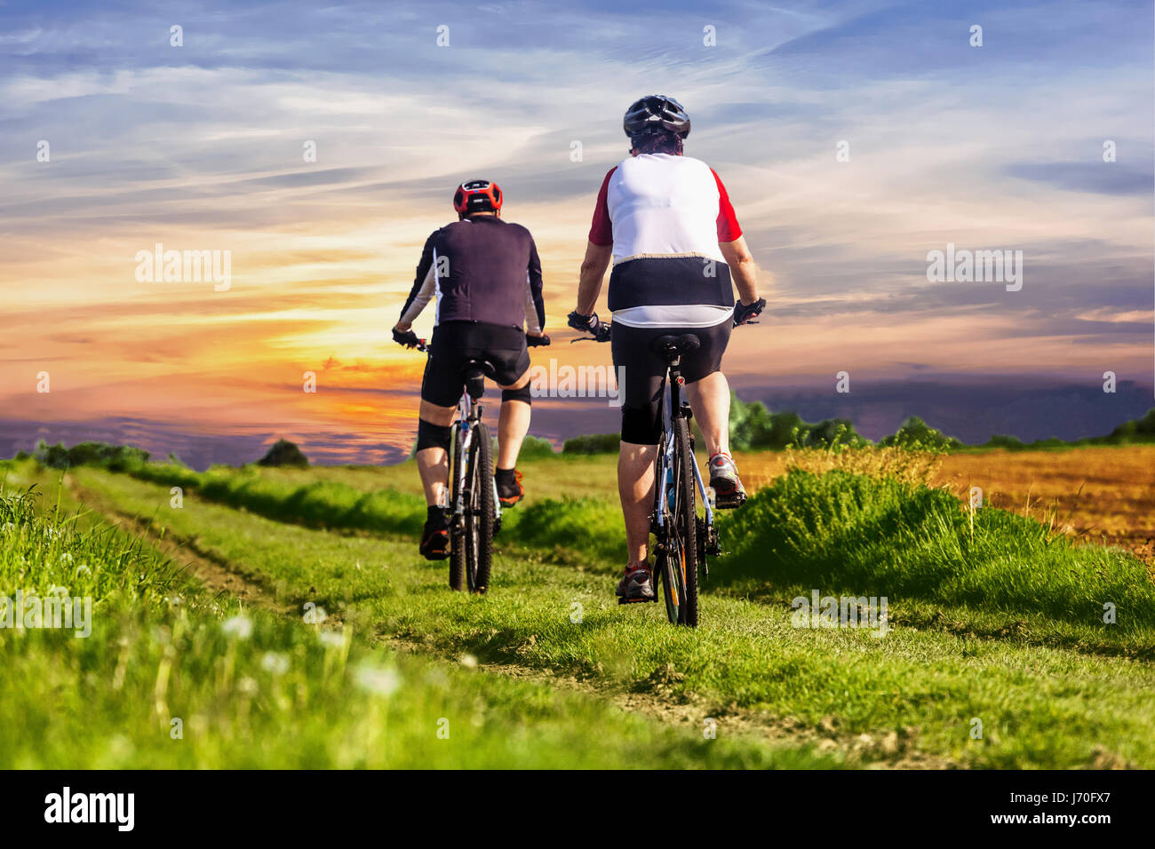 Das Paar fährt mit dem Fahrrad auf dem Feldweg Landschaft Rückansicht, Sonnenuntergang, zwei Menschen Radfahren auf der Landstraße, Land, gesunde Lebensweise Tschechische Republik Stockfoto