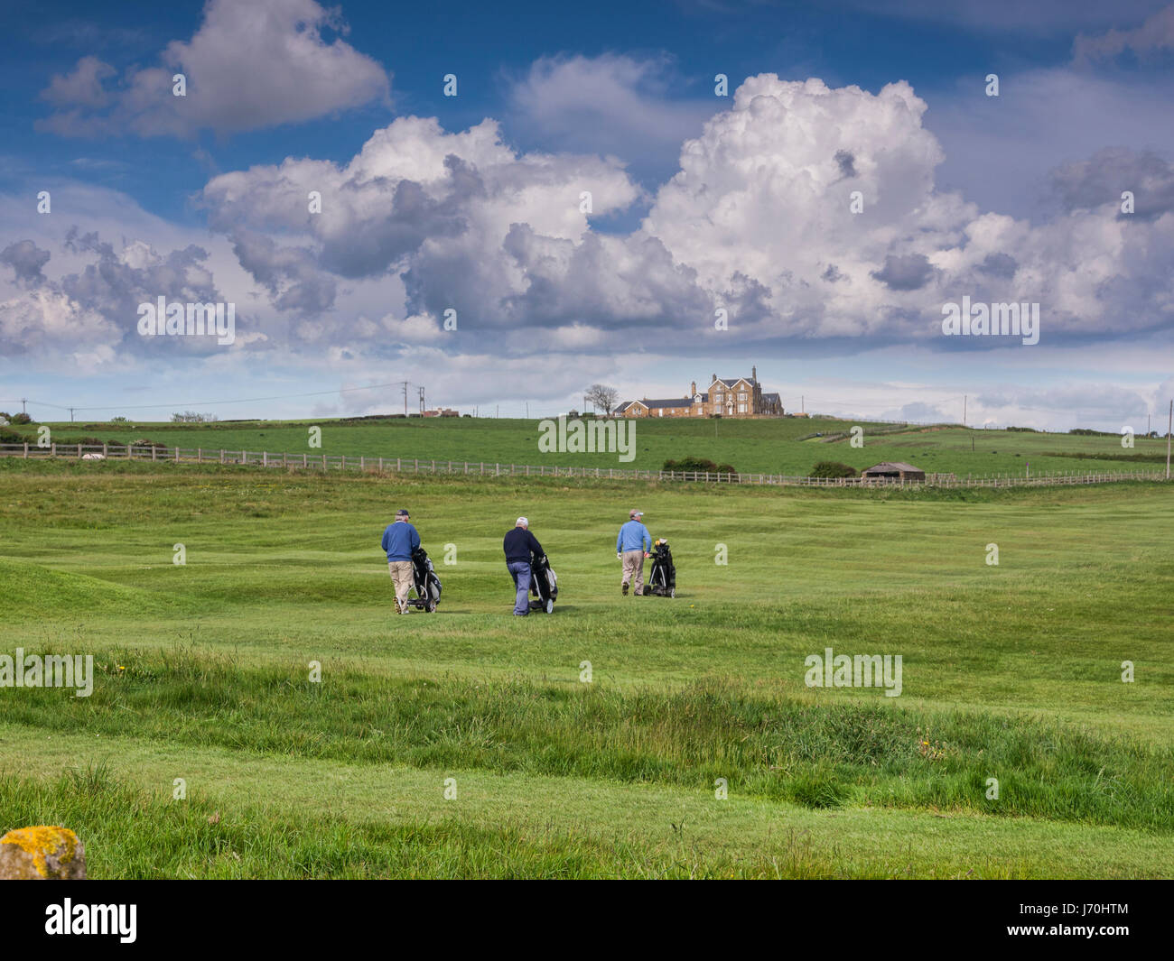 Golfer mit Rollwagen zu Fuß auf dem Golfplatz bei Whitby Golf Club, North Yorkshire, England, UK Stockfoto