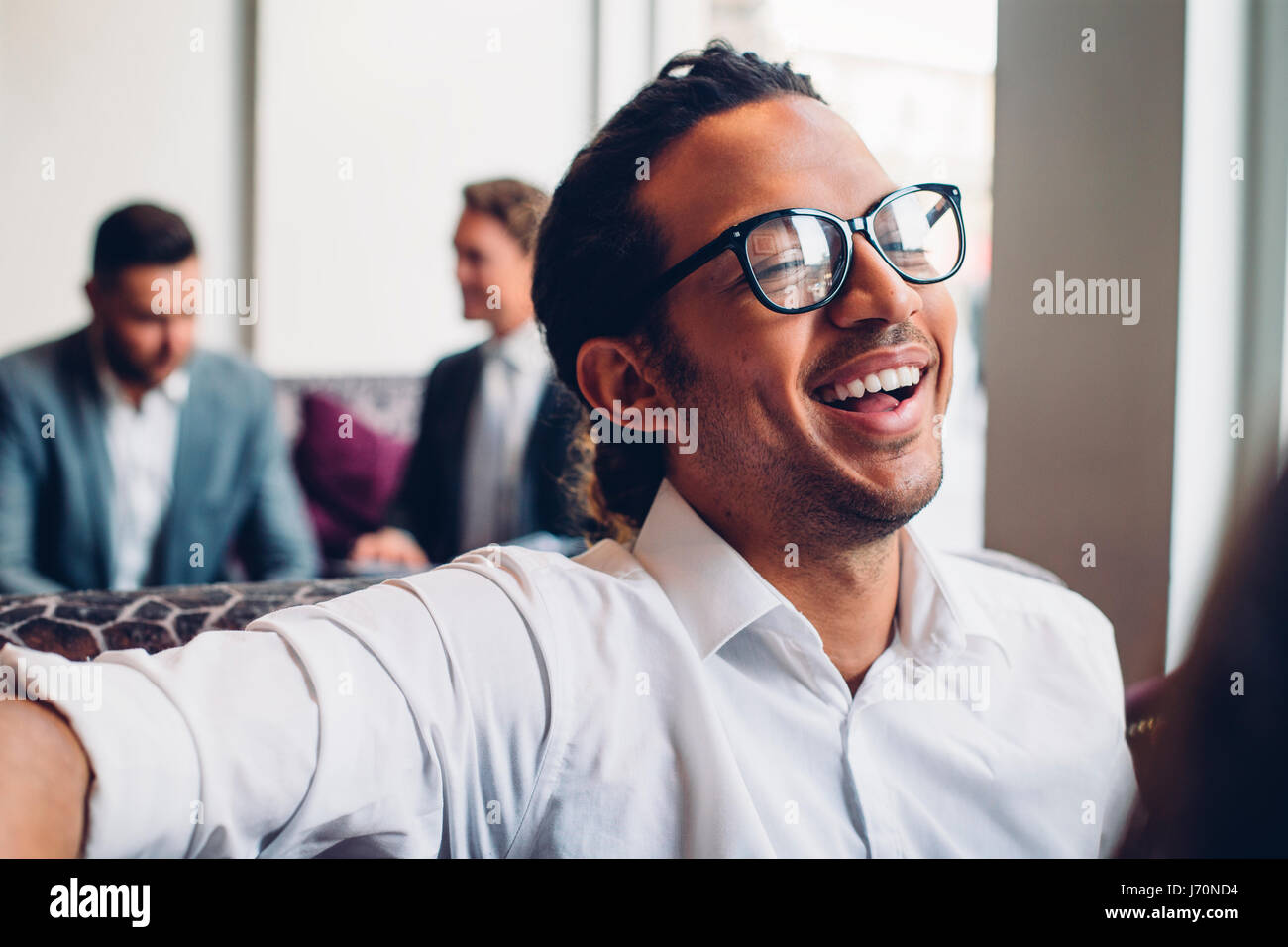 Aufnahme eines Geschäftsmannes in einem Gespräch mit jemanden lachen hautnah. Zwei Männer in Anzügen können reden im Hintergrund gesehen werden. Stockfoto