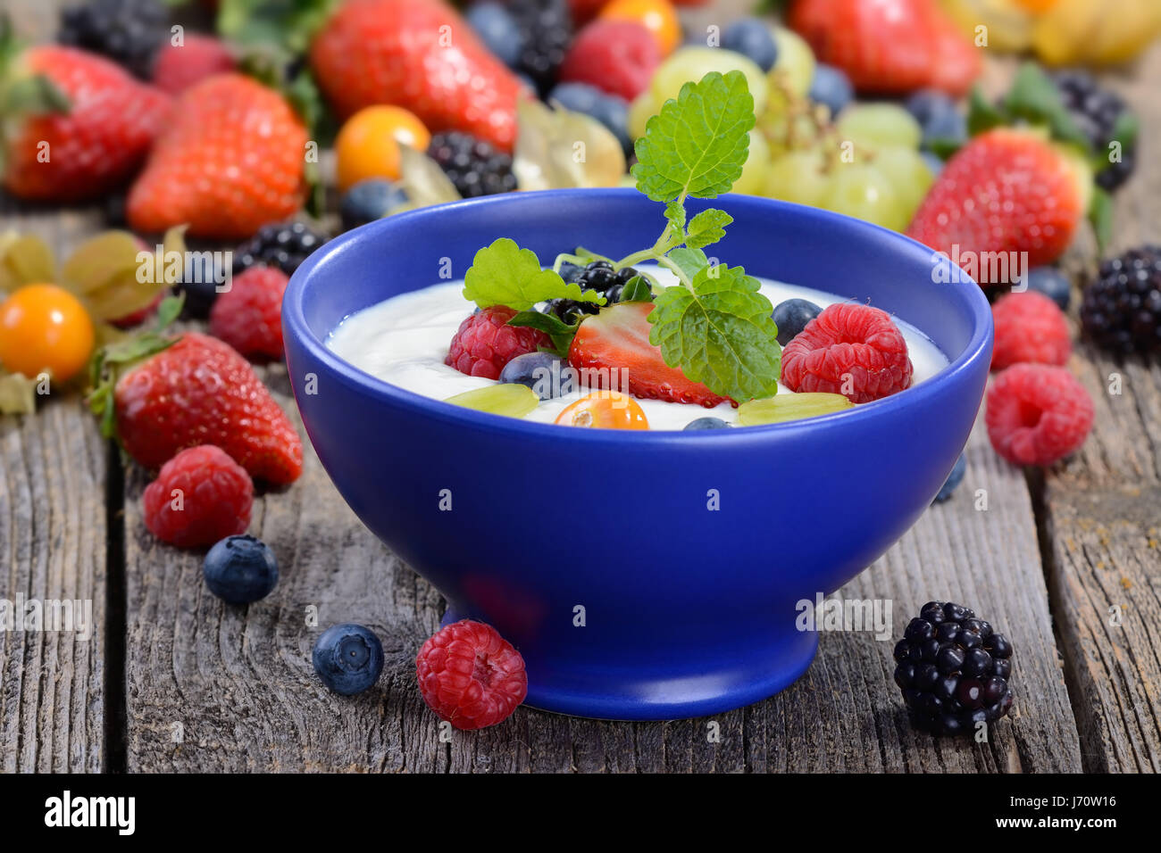 Joghurt mit gemischten frischen Früchten in einem blauen Keramikschale auf einem Holztisch Stockfoto