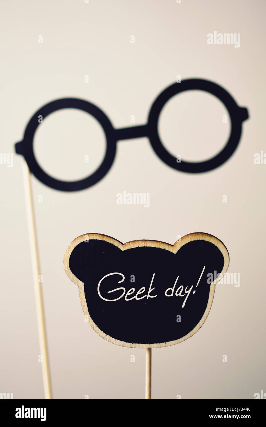 ein paar Runde-gerahmte Brille befestigt einen Holzgriff und den Text Geek-Tag in einem schwarzen Schild auf eine wollweiße Hintergrund geschrieben Stockfoto