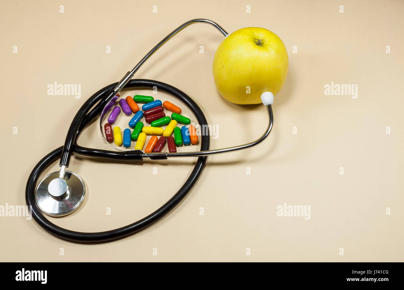 Goldener Apfel Obst zwischen den metallischen Teilen der medizinische Stethoskop mit farbigen Pillen beiseite, Ernährung und gesunde Ernährung Konzept Stockfoto