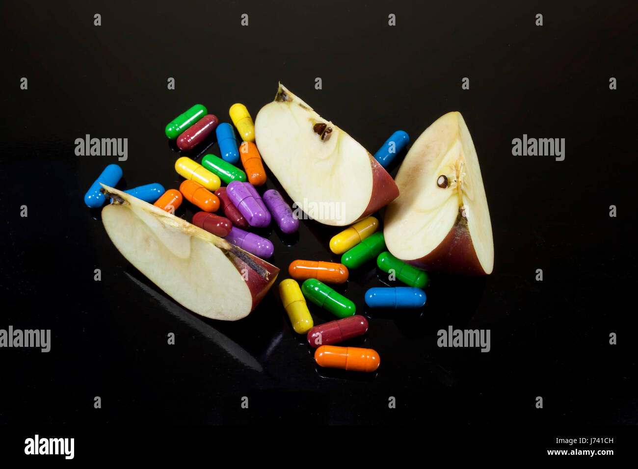 Scheiben von rotem Apfel, umgeben von bunten Pillen oder Drogen, Konzeptbild über Ernährung und gentechnisch veränderten Lebensmitteln auf schwarzem Hintergrund Stockfoto