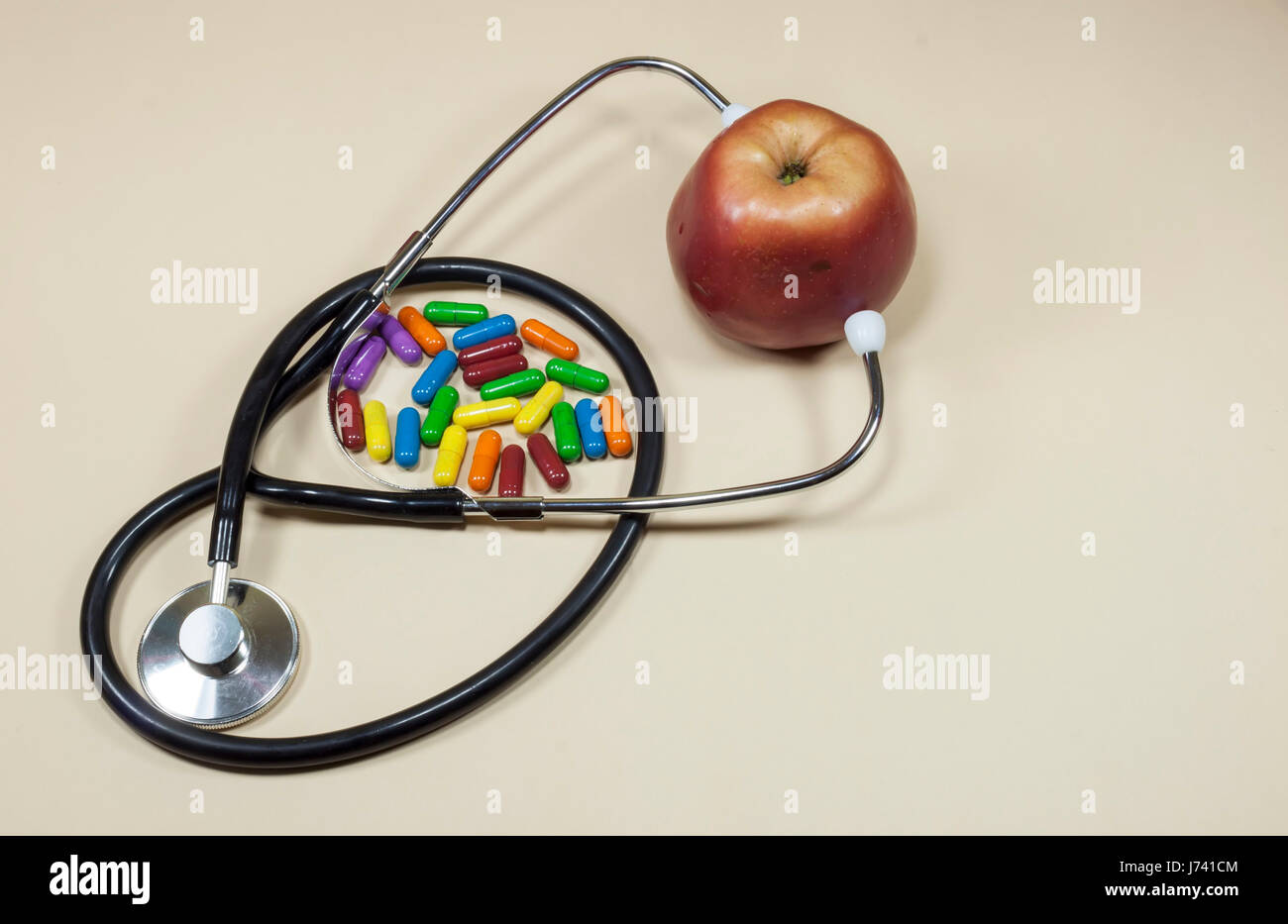 Roter Apfel Obst zwischen den Armen des medizinische Stethoskop mit farbigen Pillen beiseite, Ernährung und gesunde Ernährung und Lifestyle-Konzept Stockfoto