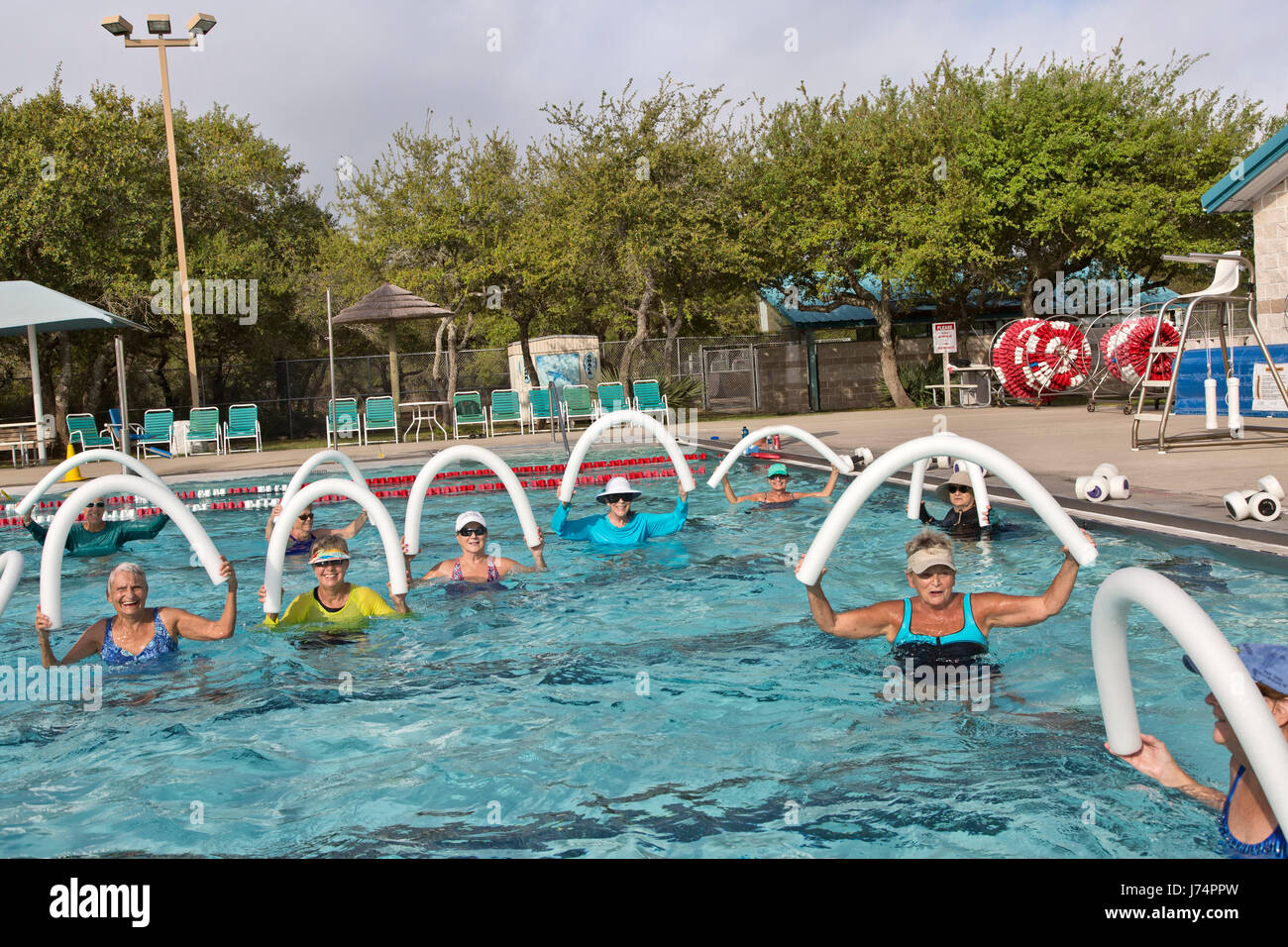 Gruppe des Lächelns glücklicher Frauen in Führungspositionen Teilnahme an Wasser-Aerobic-Kurs, mit Styropor "Wasser Nudeln", beheizten Außenpool. Stockfoto