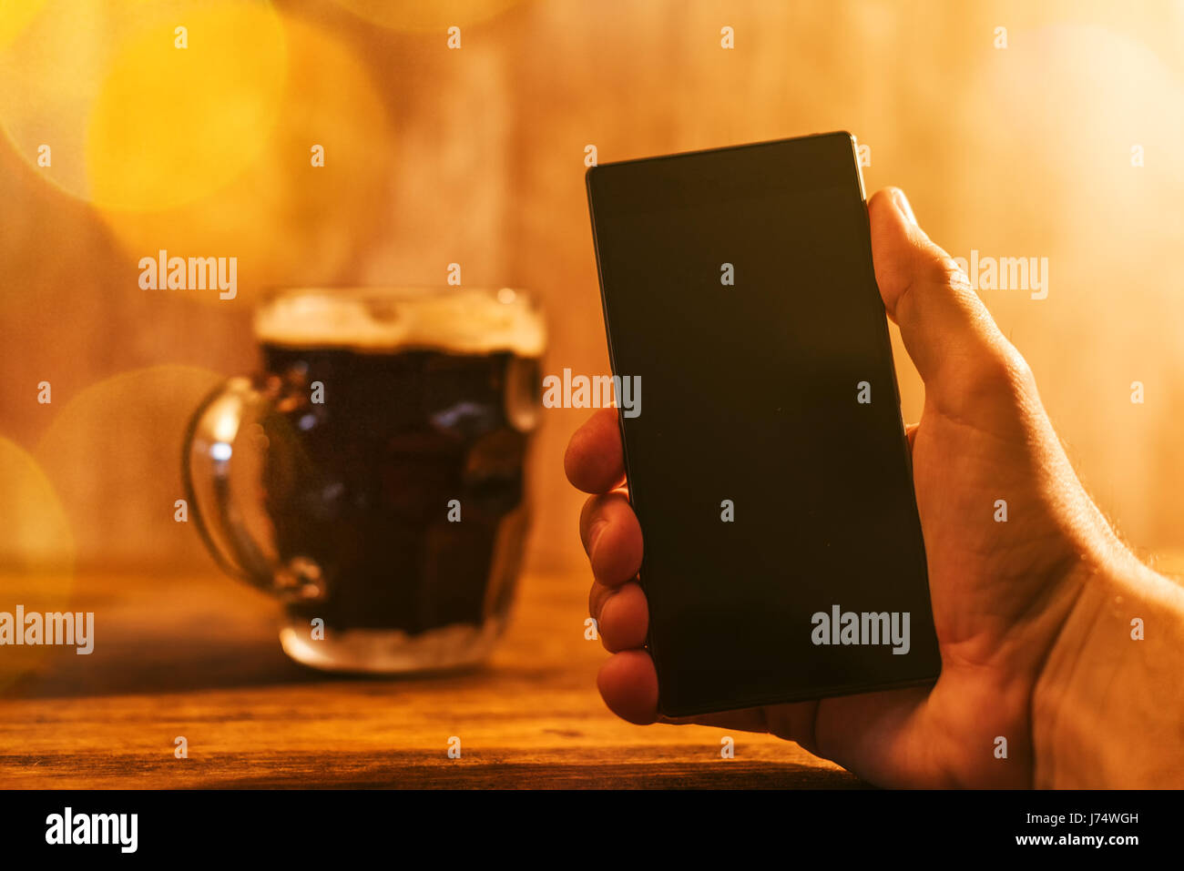 Mann mit Handy und dunklen Bierkrug in der Bar sitzen, trinken Bier und mit smartphone Stockfoto