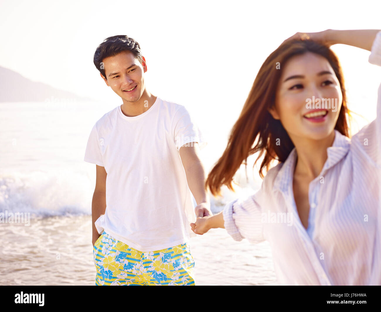 junge liebevolle und glückliche asiatische paar halten die Hände auf Strand. Stockfoto
