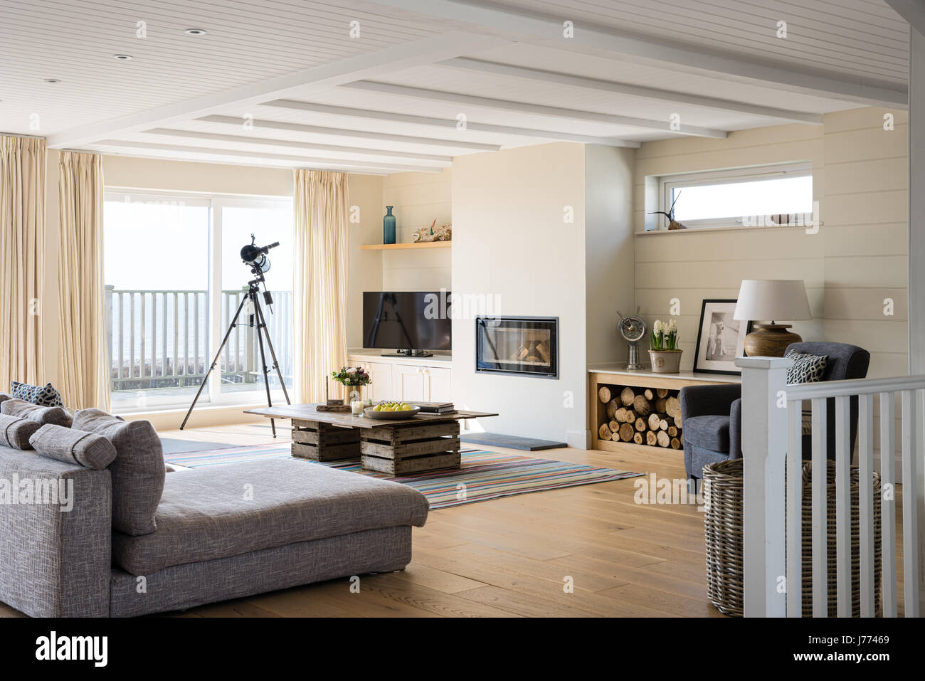 Lichtdurchfluteten Wohnzimmer mit Balkon und Teleskop. Der Couchtisch  besteht aus alten Apple-Kisten und das modulare Sofa ist grau  Stockfotografie - Alamy