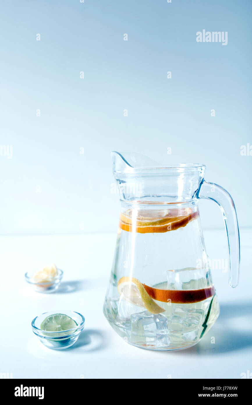 Zitrusfrüchte-Scheiben mit Wasser im Krug auf Tisch gegen Wand Stockfoto