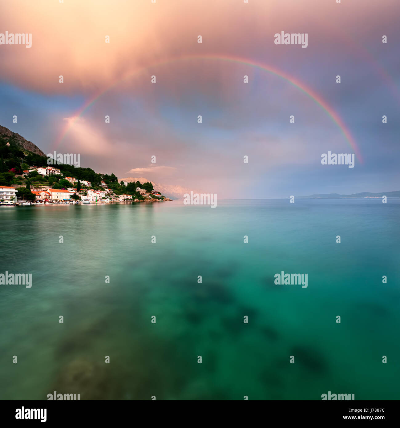 Regenbogen über felsigen Strand und kleine Dorf nach dem Regen, Dalmatien, Kroatien Stockfoto