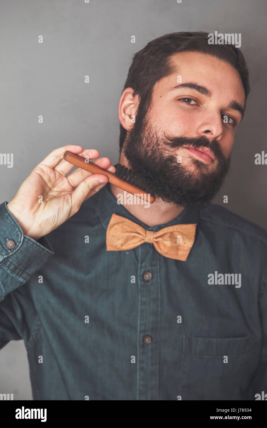 Mann, der seinen Bart mit einer hölzernen Bürste Kämmen trägt Denim Shirt und Kork Fliege Stockfoto