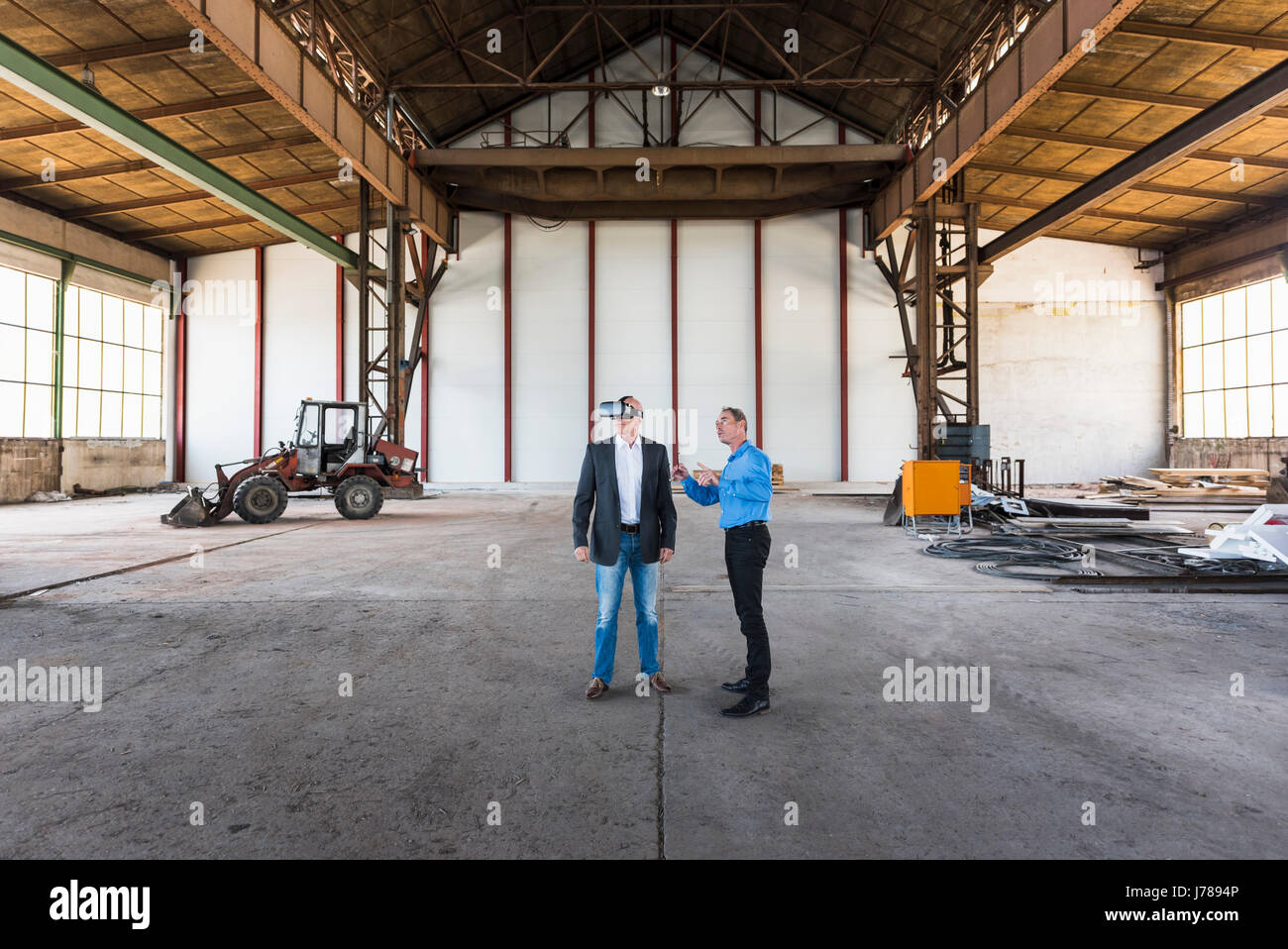 Zwei Geschäftsleute mit VR-Brille in alten Industriehalle im Gespräch Stockfoto