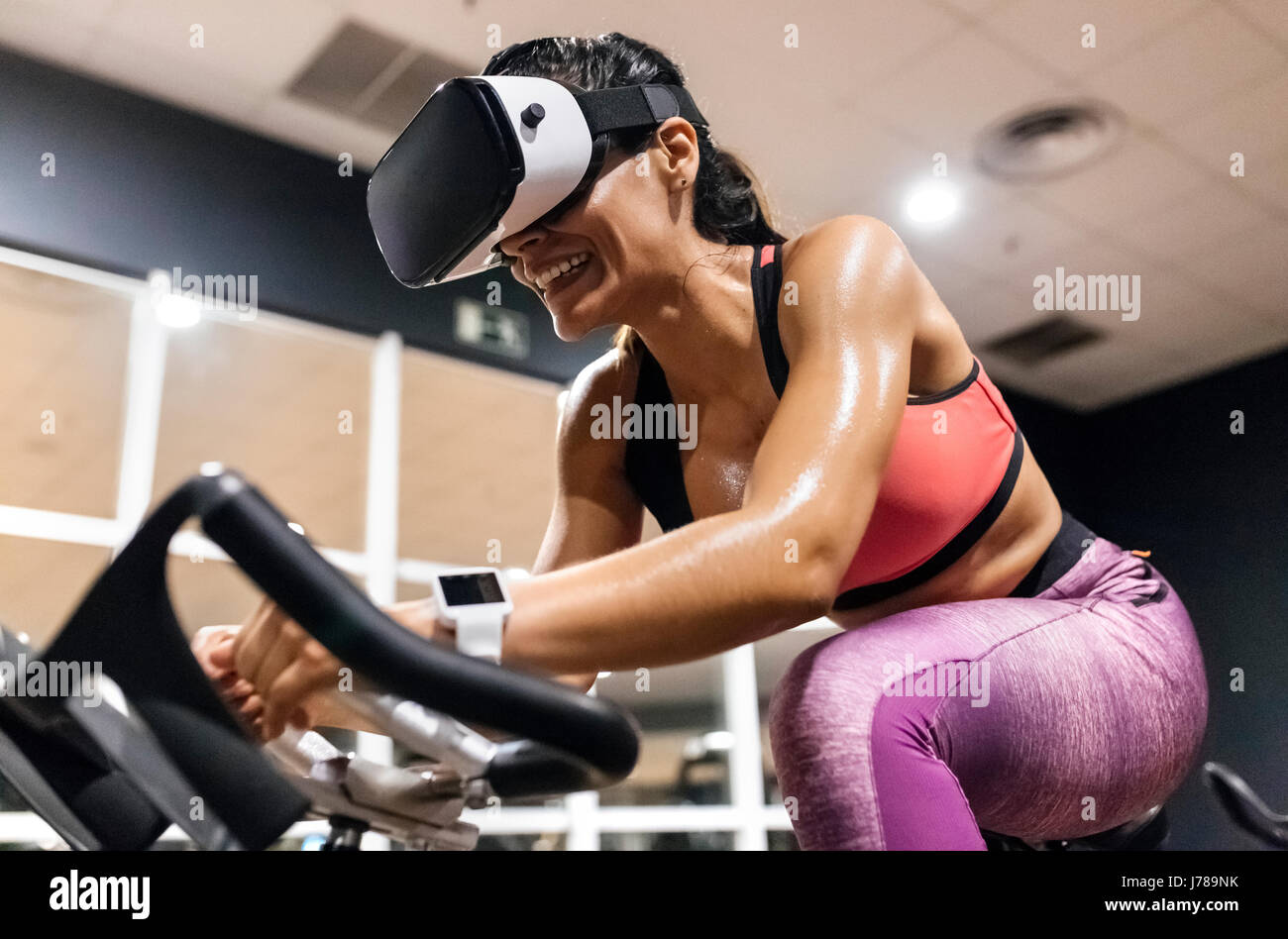 Frau mit VR-Brille auf Spinning-Bike in der Turnhalle Stockfoto