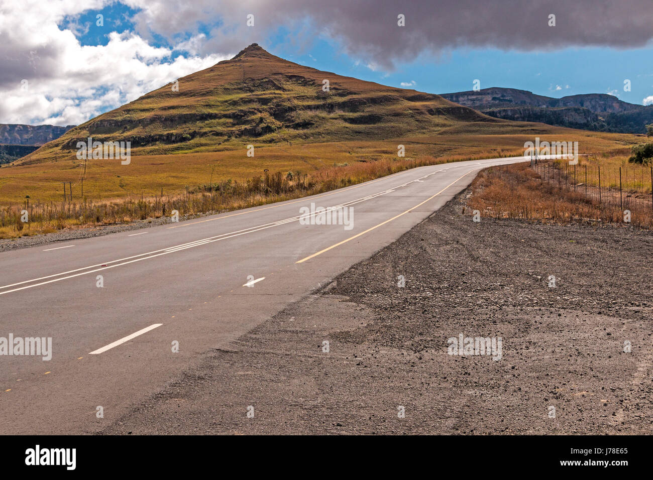 Gebogene leer ländlichen Asphaltstraße durch trockenen Winter Berglandschaft gegen blauen Wolke Himmel Horizont n Orange Free State in Südafrika Stockfoto