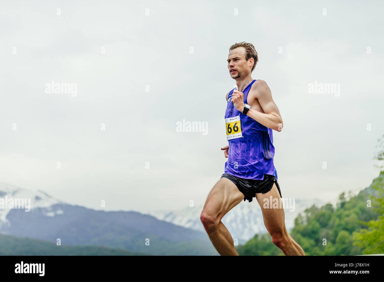 junge männliche Läufer auf Hintergrund Himmel und Berge im Rennen Spring Mountain Marathon laufen Stockfoto