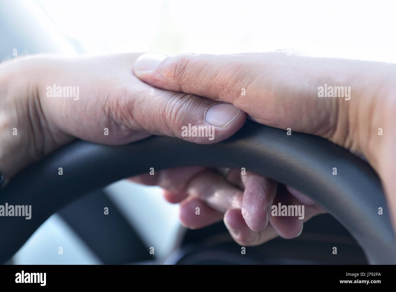 Müde Hände eines älteren Mannes am Lenkrad eines Autos gegen die Morgensonne Stockfoto