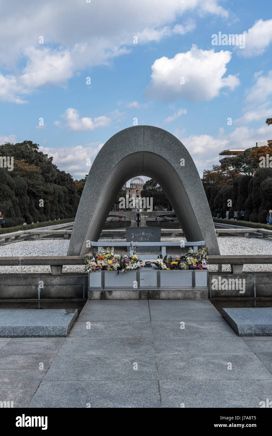 Die Hiroshima-Kenotaph, framing A-Dome und die Flamme des Friedens.  Ein paar Leute sitzen und stehen rund um den Teich des Friedens. Stockfoto