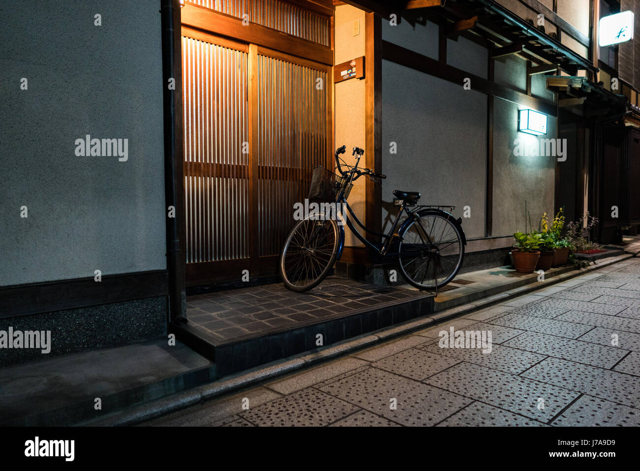 Ein Fahrrad bleibt vor einem Haus in der Nacht freigeschaltet. Die Tür erfolgt mit dünnen Holzleisten, so dass die Innenbeleuchtung zu sickern. Stockfoto