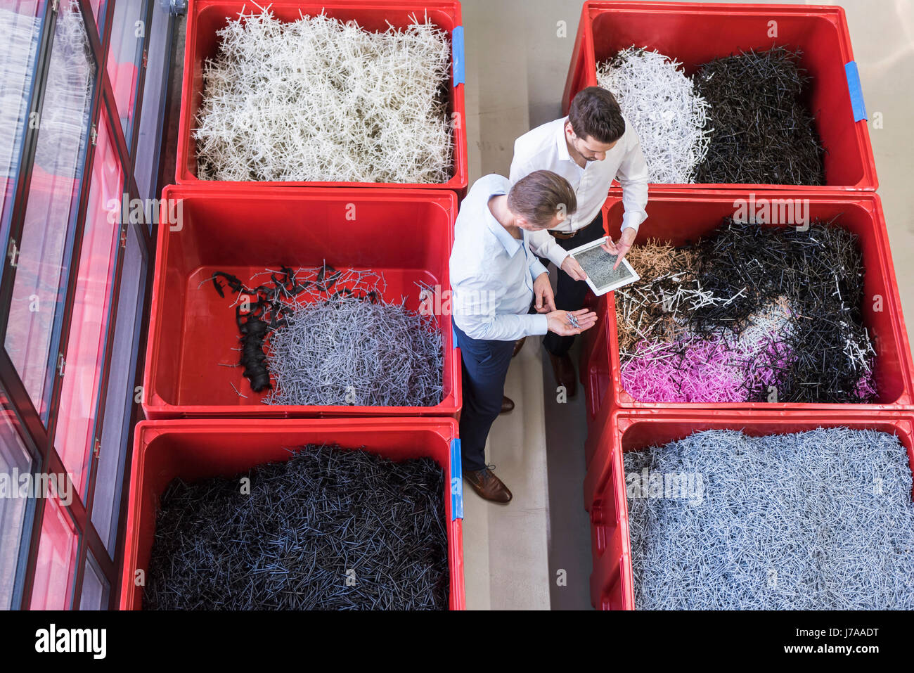 Zwei Geschäftsleute mit Tablette in der Fabrik stehen bei Behältern mit Fetzen Stockfoto