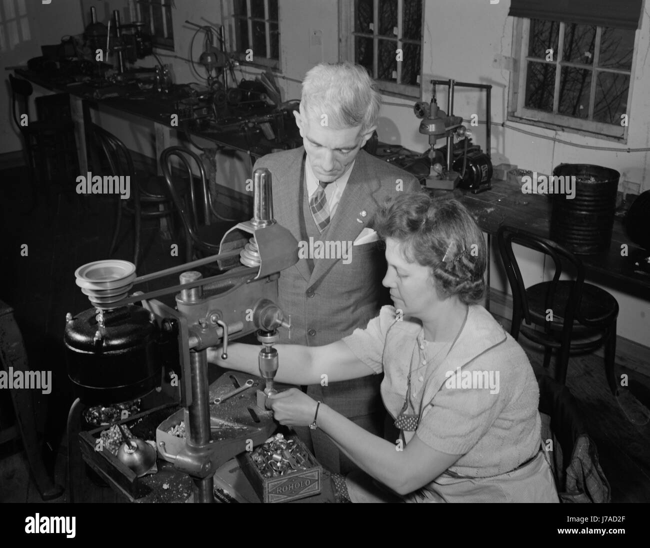Frau Maschinist platziert Schrauben in elektrische Terminal wie ihr Vorgesetzter, 1942 aussieht. Stockfoto