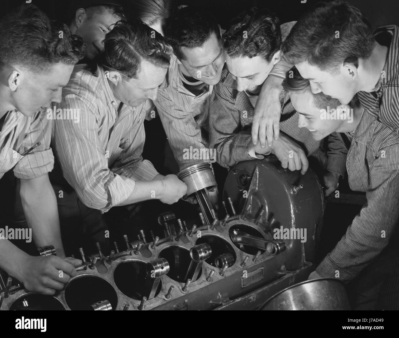 Lehrer zeigt einer Gruppe von Männern, wie einen Flugzeugmotor zusammenzubauen. Stockfoto