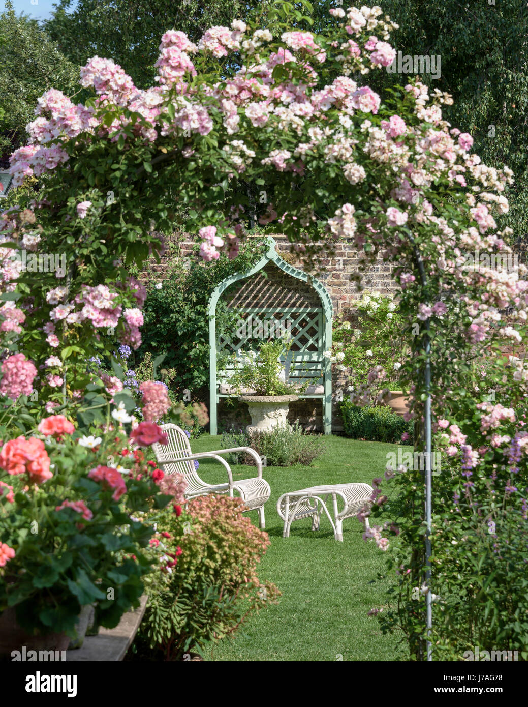 Wicker Gartenmöbel durch einen rose Bogen in einen englischen Garten zu sehen. Stockfoto