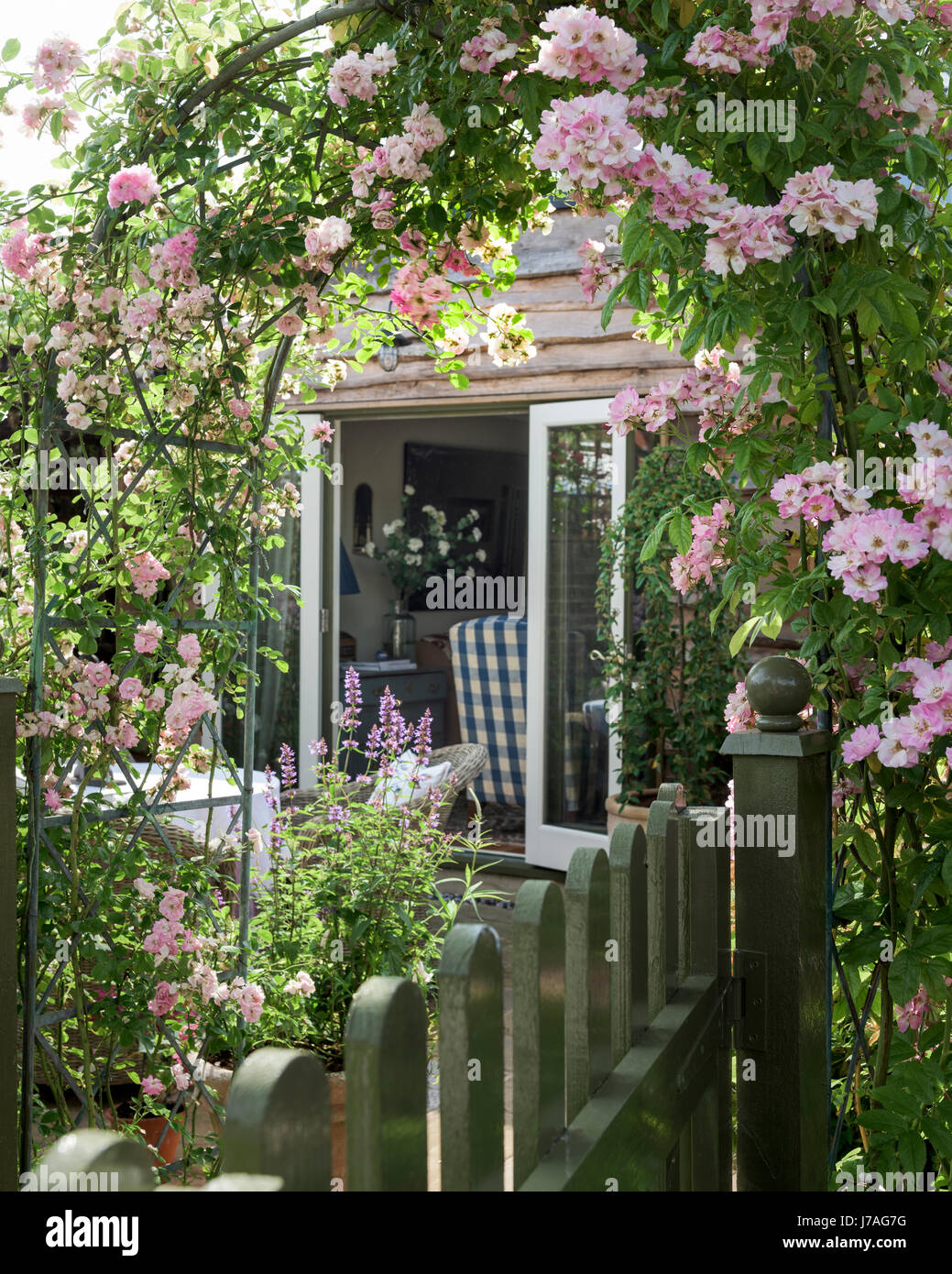 Durch den Garten rose Arch zu Eichen bewachsenen Wohnhauserweiterung mit französischen Fenstern anzeigen Stockfoto