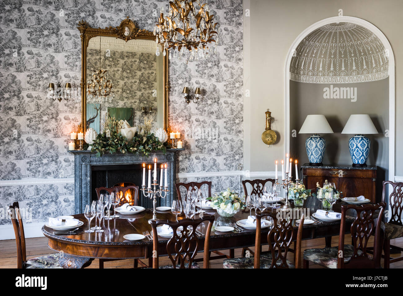 Esszimmer mit Glas und vergoldeten Kronleuchter aus JFM Innenräume über Esstisch für eine formale Mahlzeit gelegt. Ein großer vergoldeter Spiegel liegt über dem Kaminsims Stockfoto