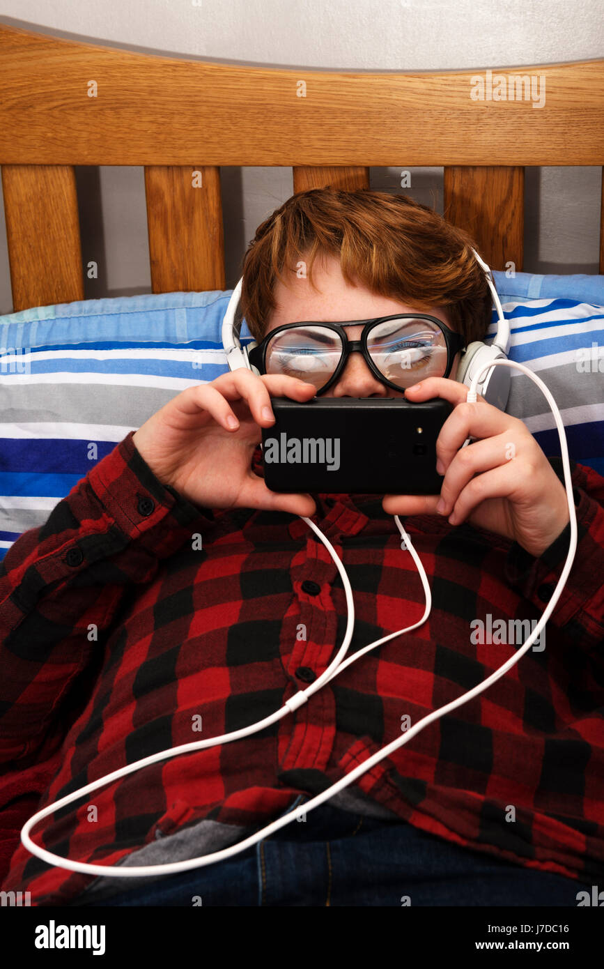 11-jährige junge im Schlafzimmer mit einem Smartphone im Internet surfen Stockfoto