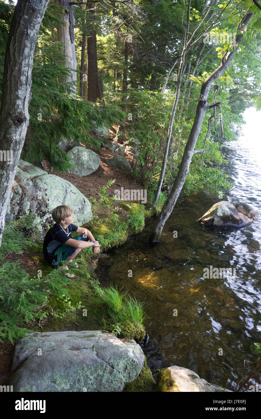 kleiner Junge sitzt am See in den Wäldern von New Hampshire Campingplätze camping Stockfoto