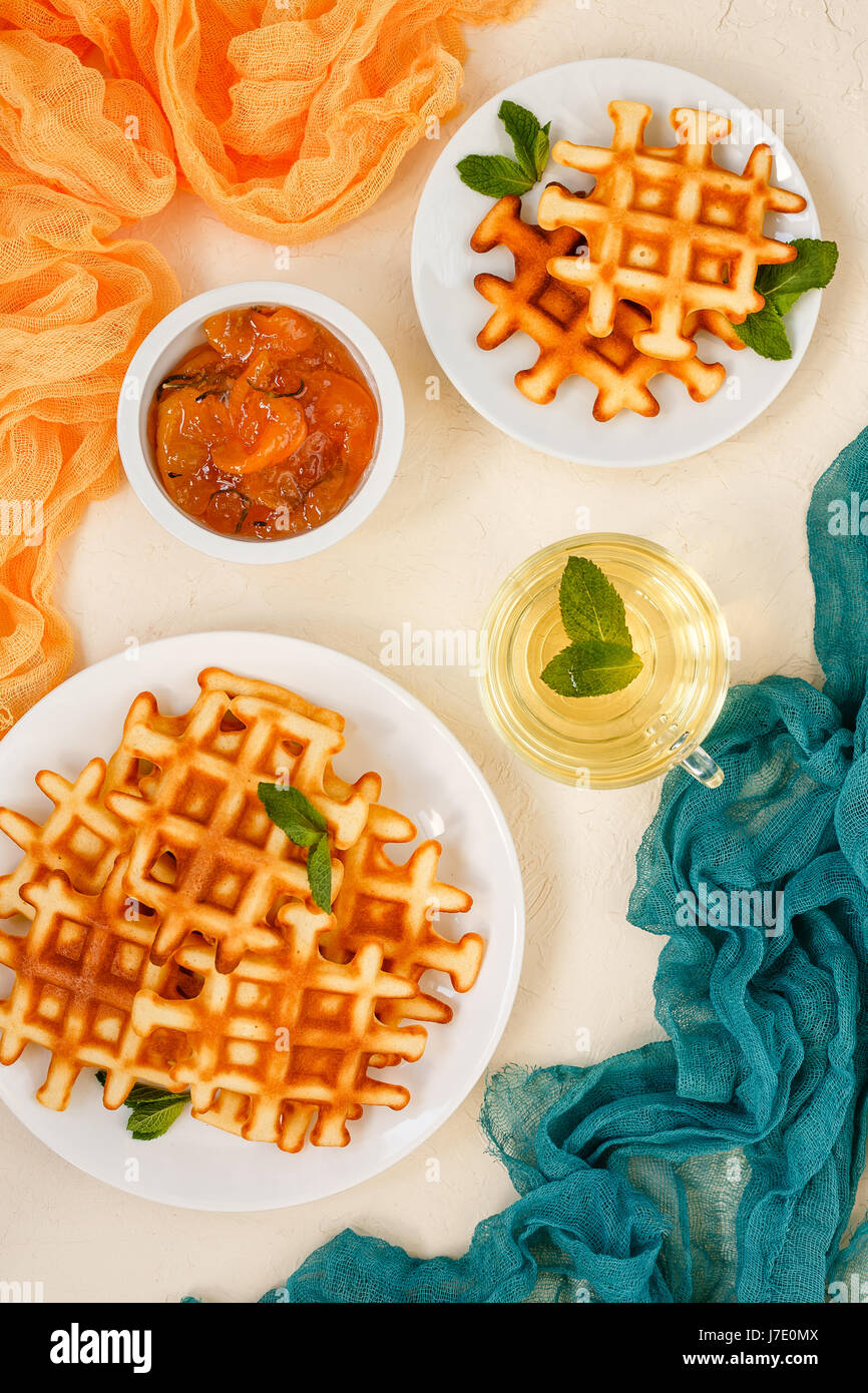 Belgische Waffeln auf Platten garniert mit Minze, Glas Tasse mit Green tea mit Minze und Pfirsichmarmelade mit Rosmarin in Schälchen auf Beige Hintergrund Stockfoto