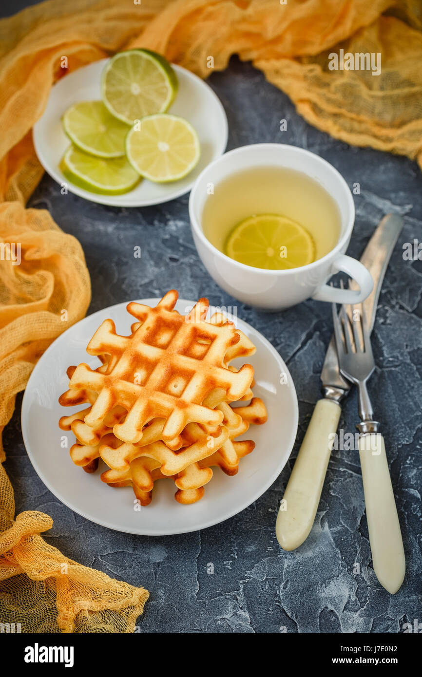 Zwei Platten mit belgischen Waffeln, Tasse mit grün, geschnitten, Kalk, Gabel mit Messer auf grauem Hintergrund. Stockfoto