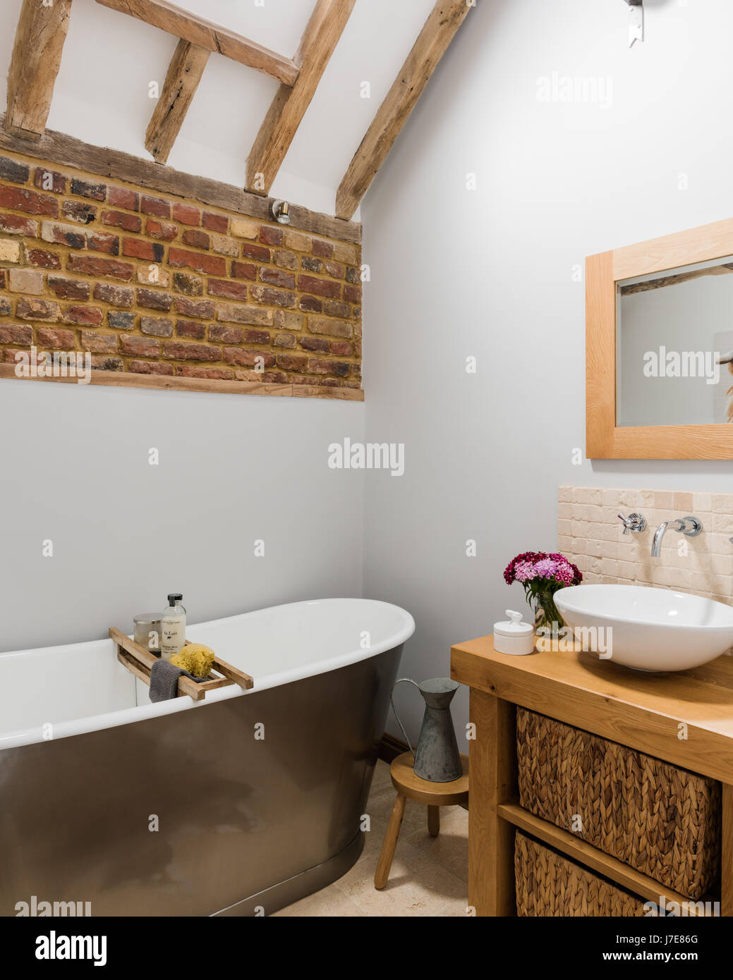 Freistehende Badewanne im rustikalen Badezimmer mit freiliegenden Ziegelwand. Die Wände sind von Albany in hellgrau lackiert. Stockfoto