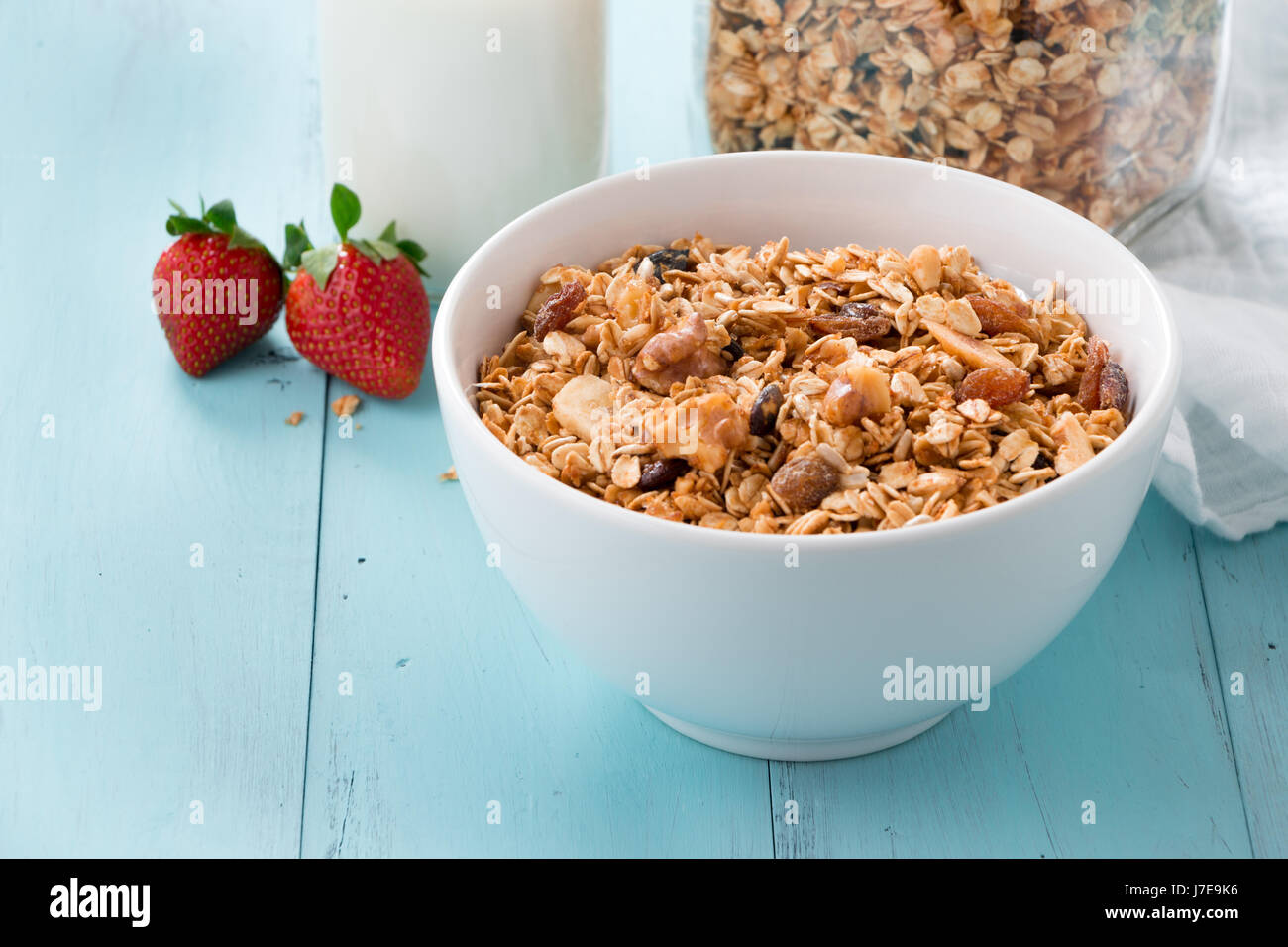 Hausgemachte gebackene Müsli in eine Schüssel geben und in ein Glas, eine Flasche Milch und Erdbeeren auf einem türkisfarbenen Holztisch. Gesundes Frühstück Stockfoto