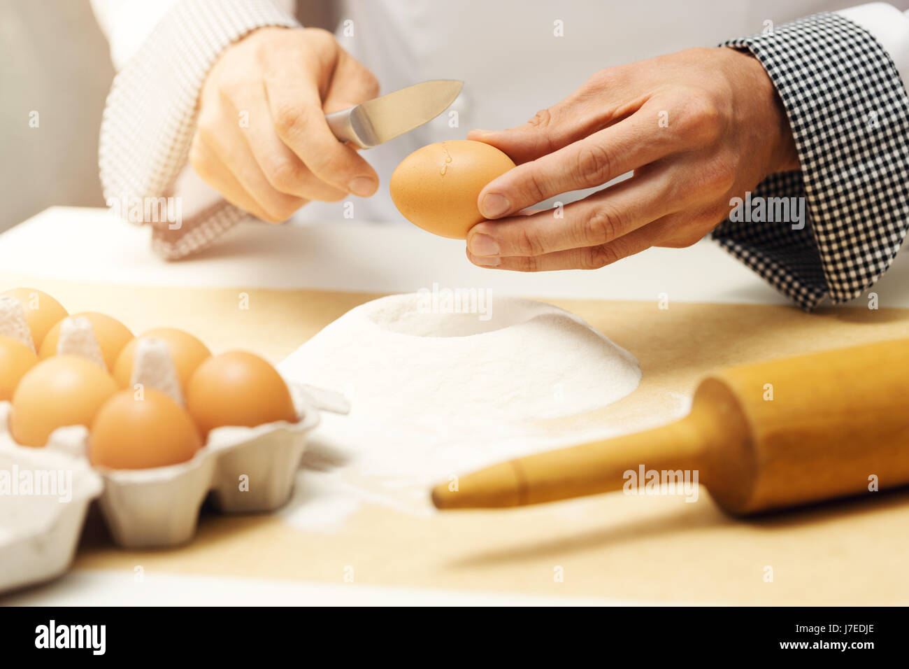 Küchenchef knacken Ei mit Messer über Mehl heap Stockfoto