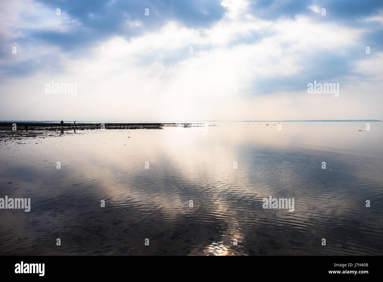 Sonne bricht durch die Wolken da Whitstable Strand ist bei Ebbe, die Schaffung einer ruhigen Spiegelung des Himmels, auf der linken Seite sind Oyster Catcher. Stockfoto