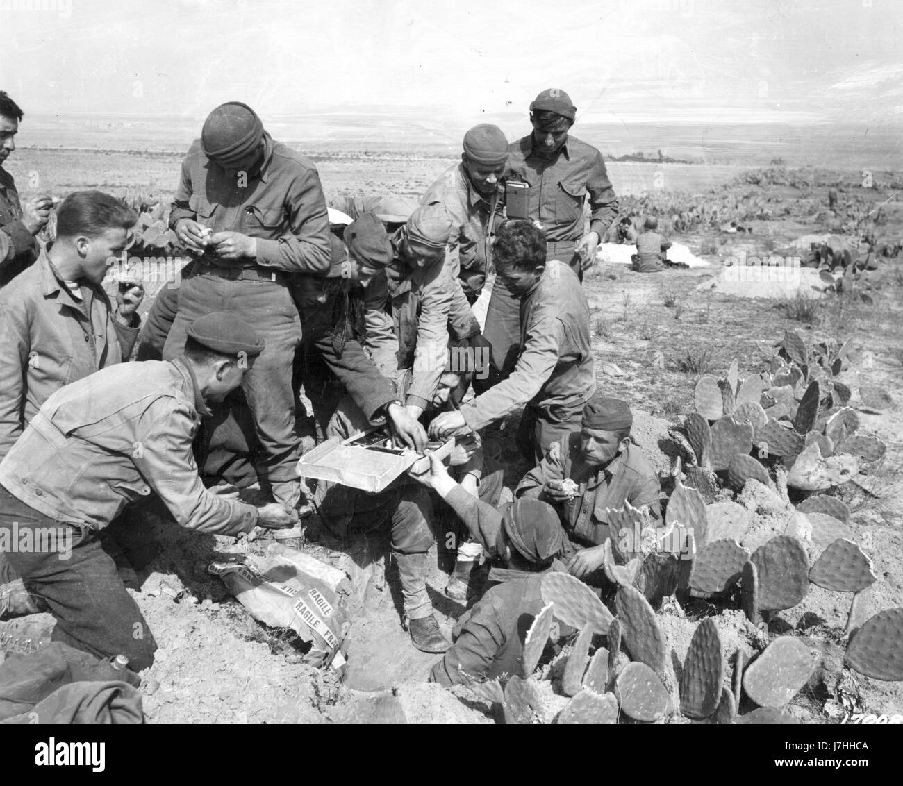 Amerikanische Fronttruppen haben US Mail von zu Hause erhalten, und ein Mann teilt sein Lebensmittelpaket mit seinen Freunden. Tunesische Wüste, Afrika WW II - 20. Februar 1943. Um meine anderen WW II-Bilder zu sehen, suchen Sie nach Prestor Vintage WW II Stockfoto