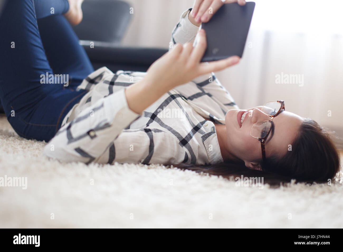 Junge Brünette Frau liegend auf Teppich zu Hause auf Tablet lesen Stockfoto