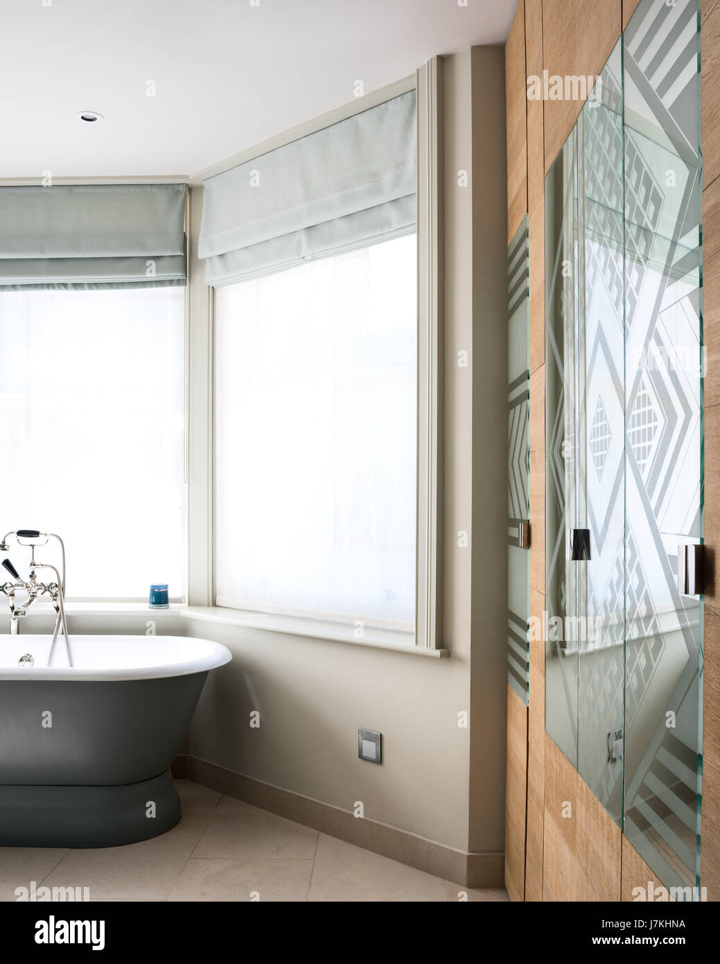 Gemusterte Spiegel Glas im Badezimmer mit freistehender Badewanne und eingebaute Schränke Stockfoto