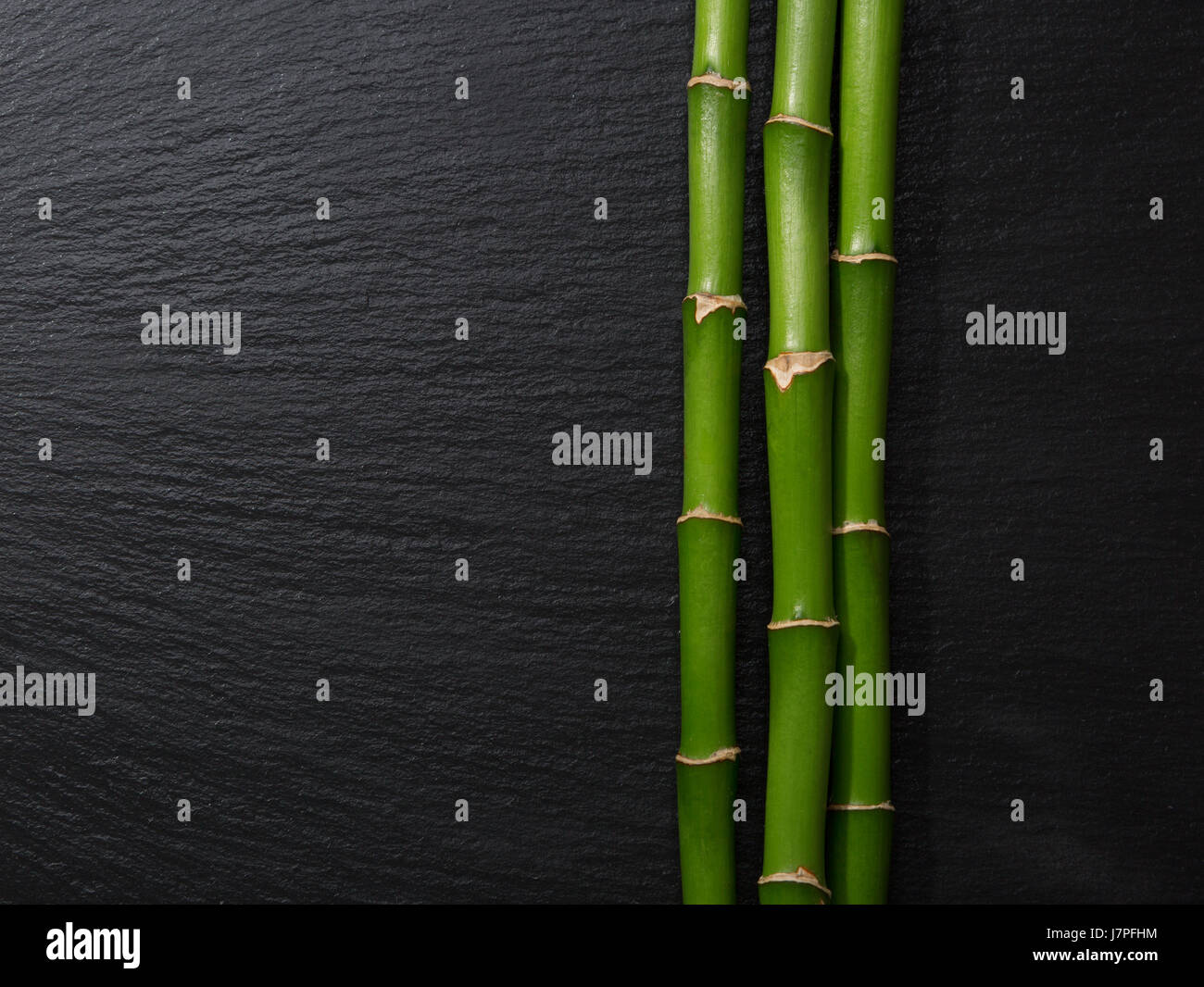 Drei Zweige der Bambus liegen auf nassen schwarzen Schiefer Stockfoto