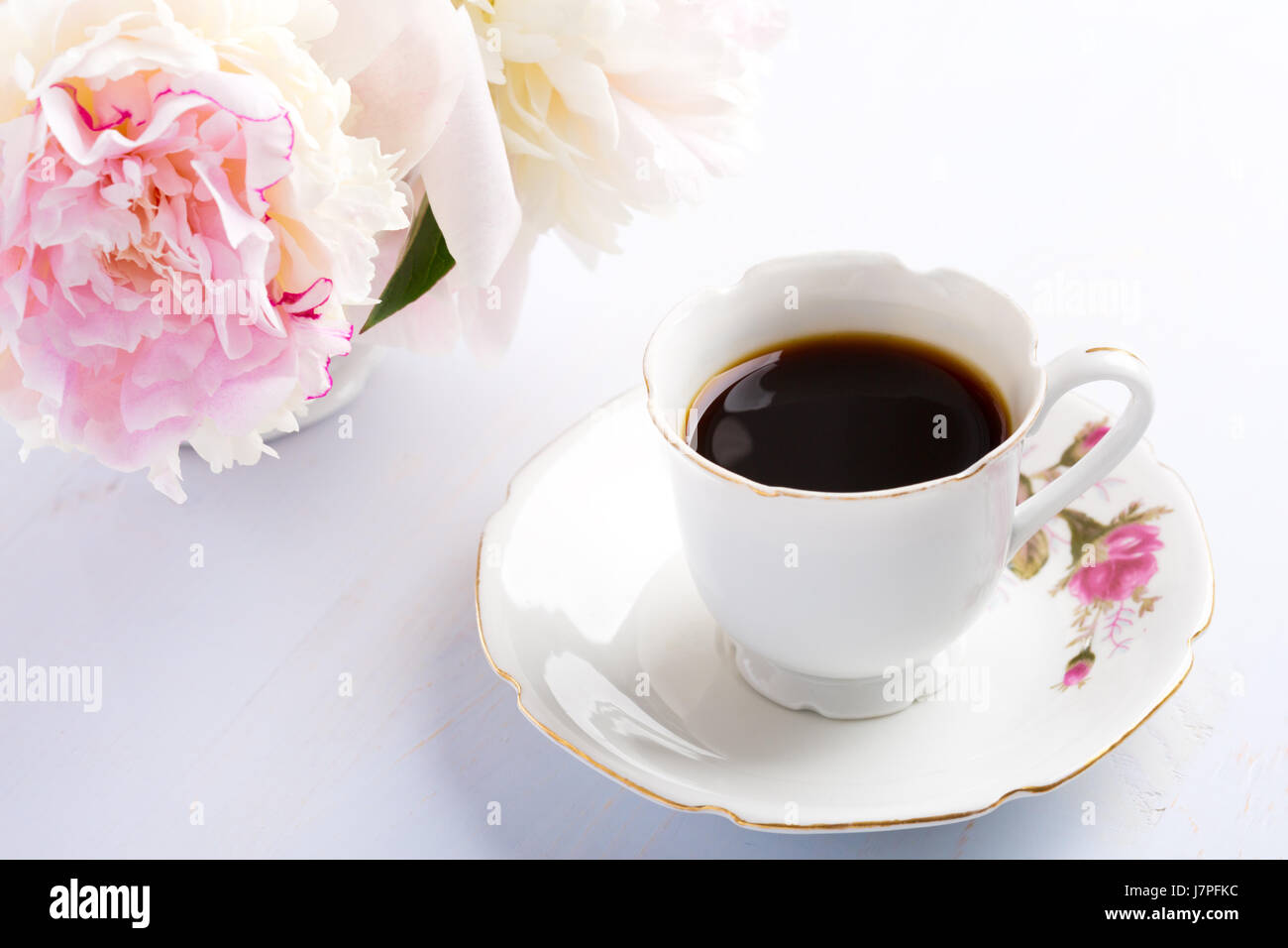 Stillleben mit Kaffee und Blumen (Pfingstrosen) auf leichten lila Holztisch. Stockfoto