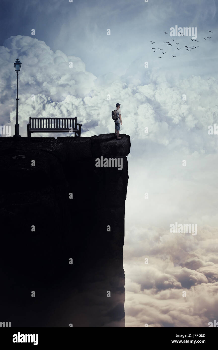 Inspirierende imaginären Blick als kleiner Junge mit einer Tasche in seinem zurück an der Spitze einer Klippe über Wolken, Blick auf den Horizont, in der Nähe einer Bank stehen. Stockfoto